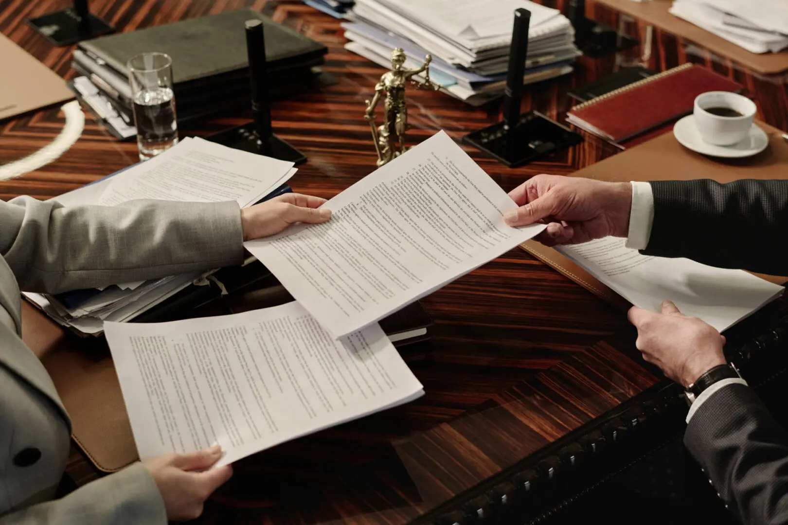 Two people exchanging legal documents at desk.