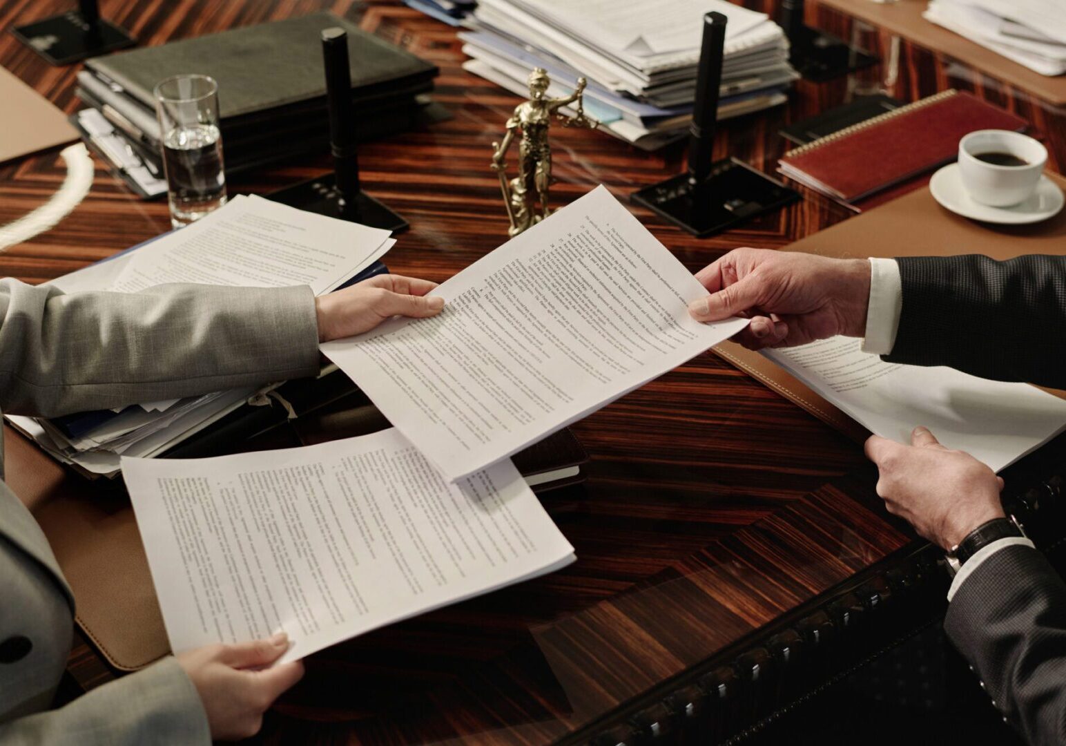 Two people exchanging legal documents at desk.